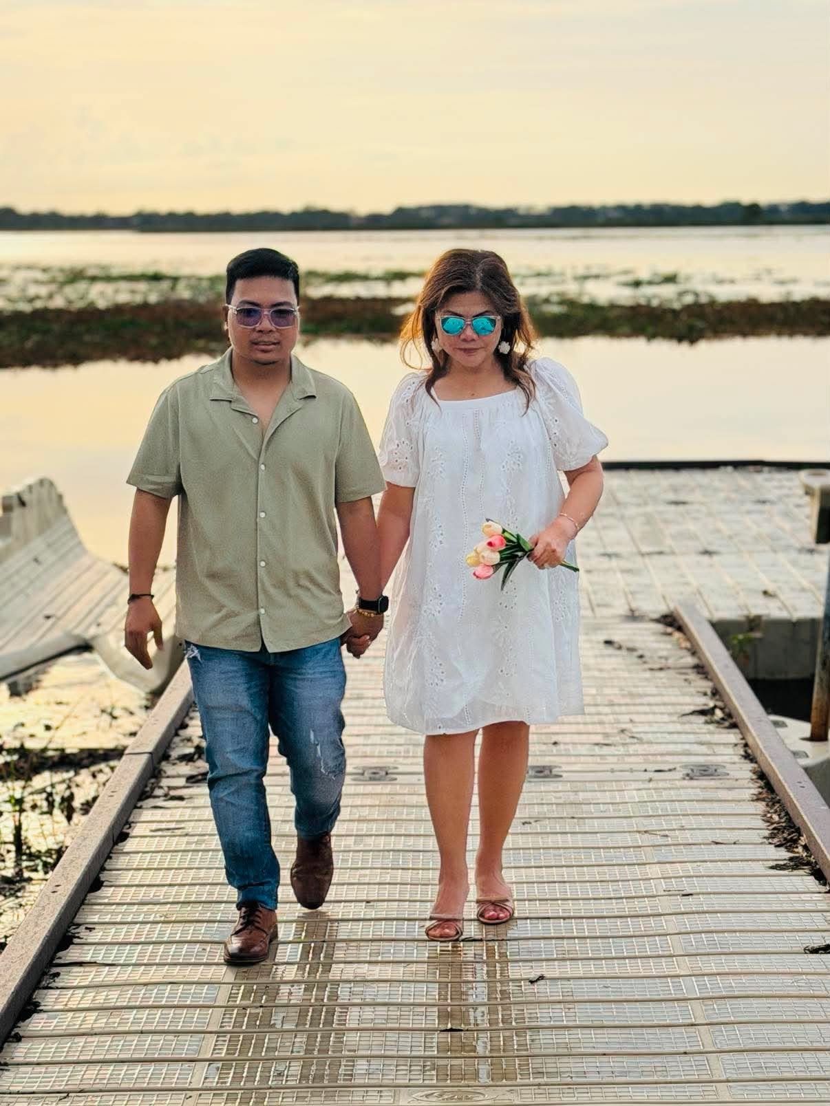Rochelle and Nathaniel walking down a lakeside boardwalk during their 2026 anniversary photoshoot