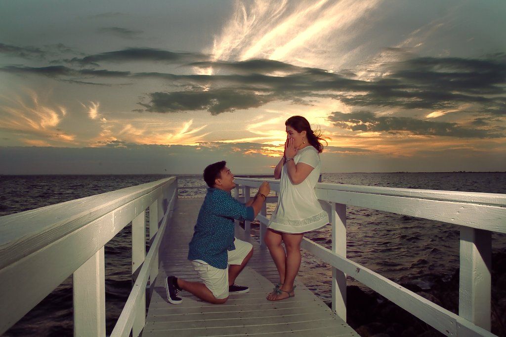 Nathaniel kneeling on a dock at sunset as he proposes to Rochelle
